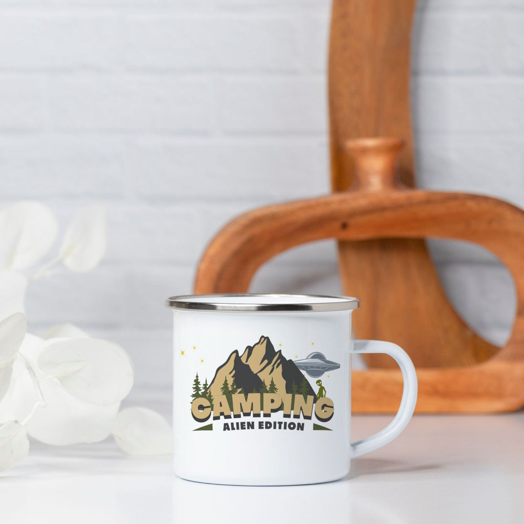 Camping-themed mug with mountain and alien design on a white surface.