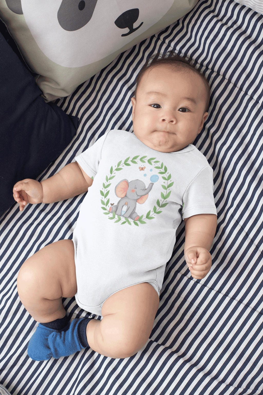 Baby wearing a onesie with a Red Rock Chaos elephant design laying on a striped blanket