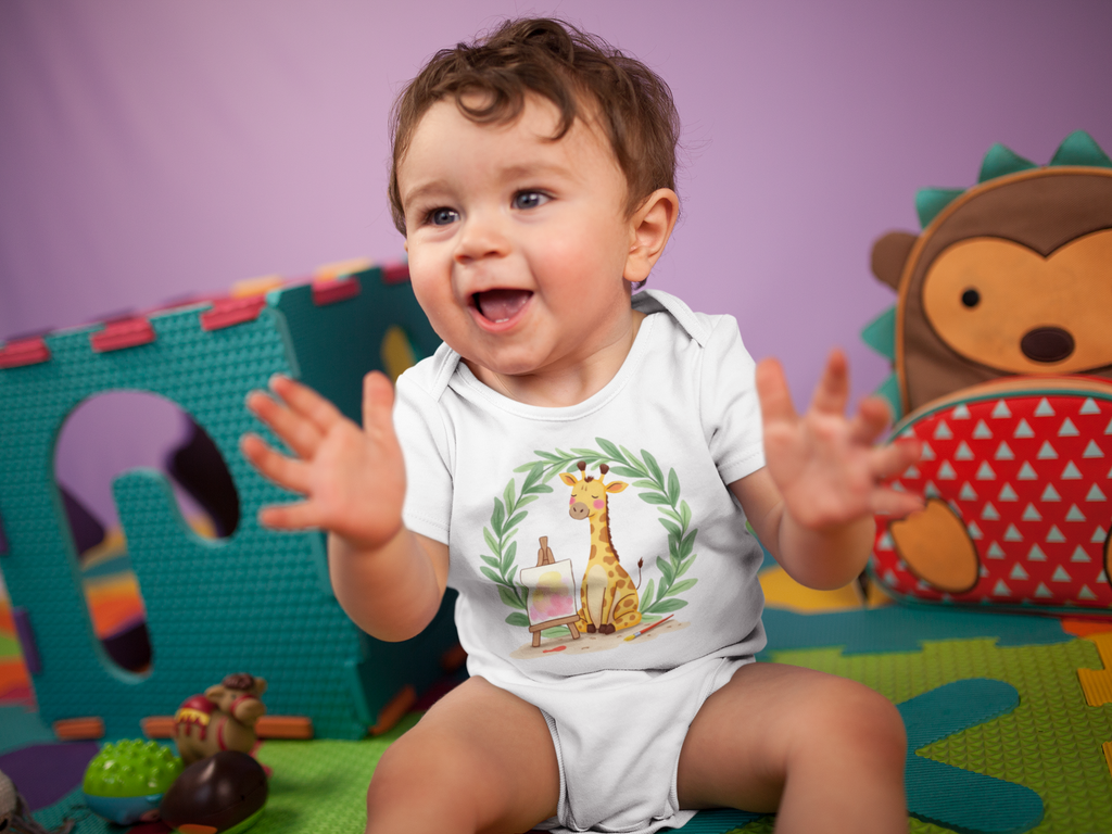 Baby sitting on a colorful play mat with toys, wearing a Little Chaos Crew giraffe sitting with eyes closed beside an easel and paintbrush inside green leafy wreath, minimalist white baby onesie design.