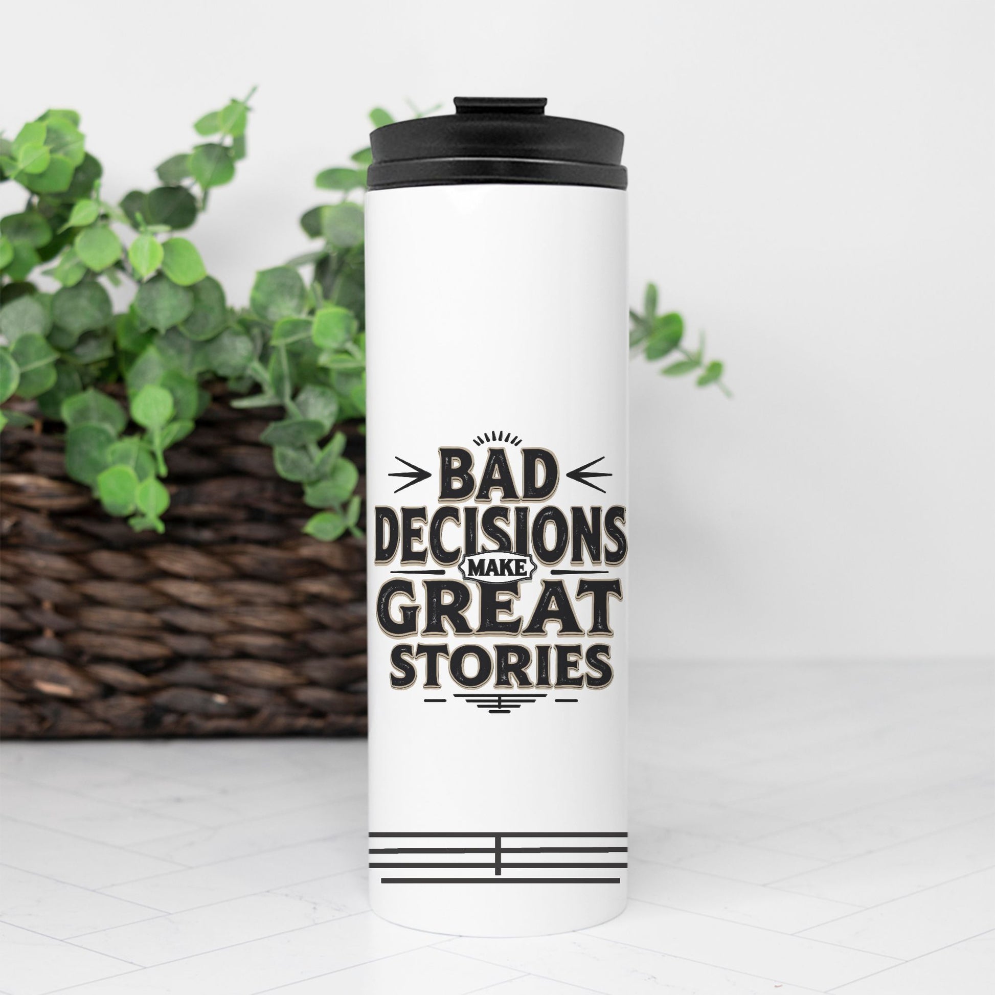 White tumbler with 'Bad Decisions Make Great Stories' text on a white background with greenery.