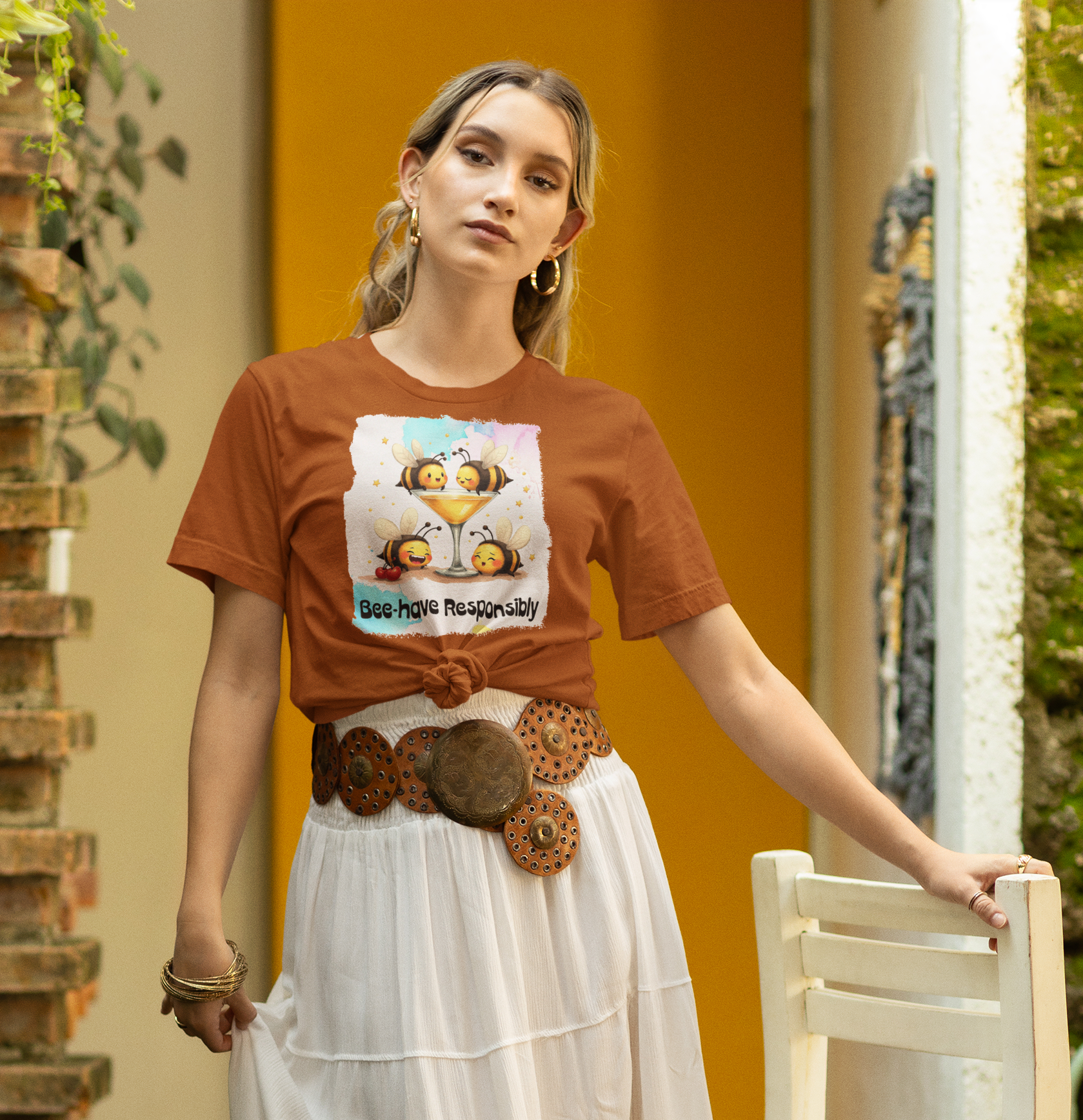 Woman wearing a brown t-shirt with a graphic design and a white skirt, standing in an outdoor setting.
