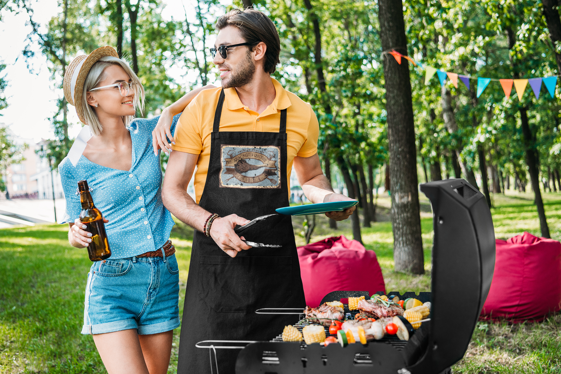 Man in an apron that says, "Certified Grill Master" grilling food outdoors with a woman holding a beer, surrounded by trees and a banner.