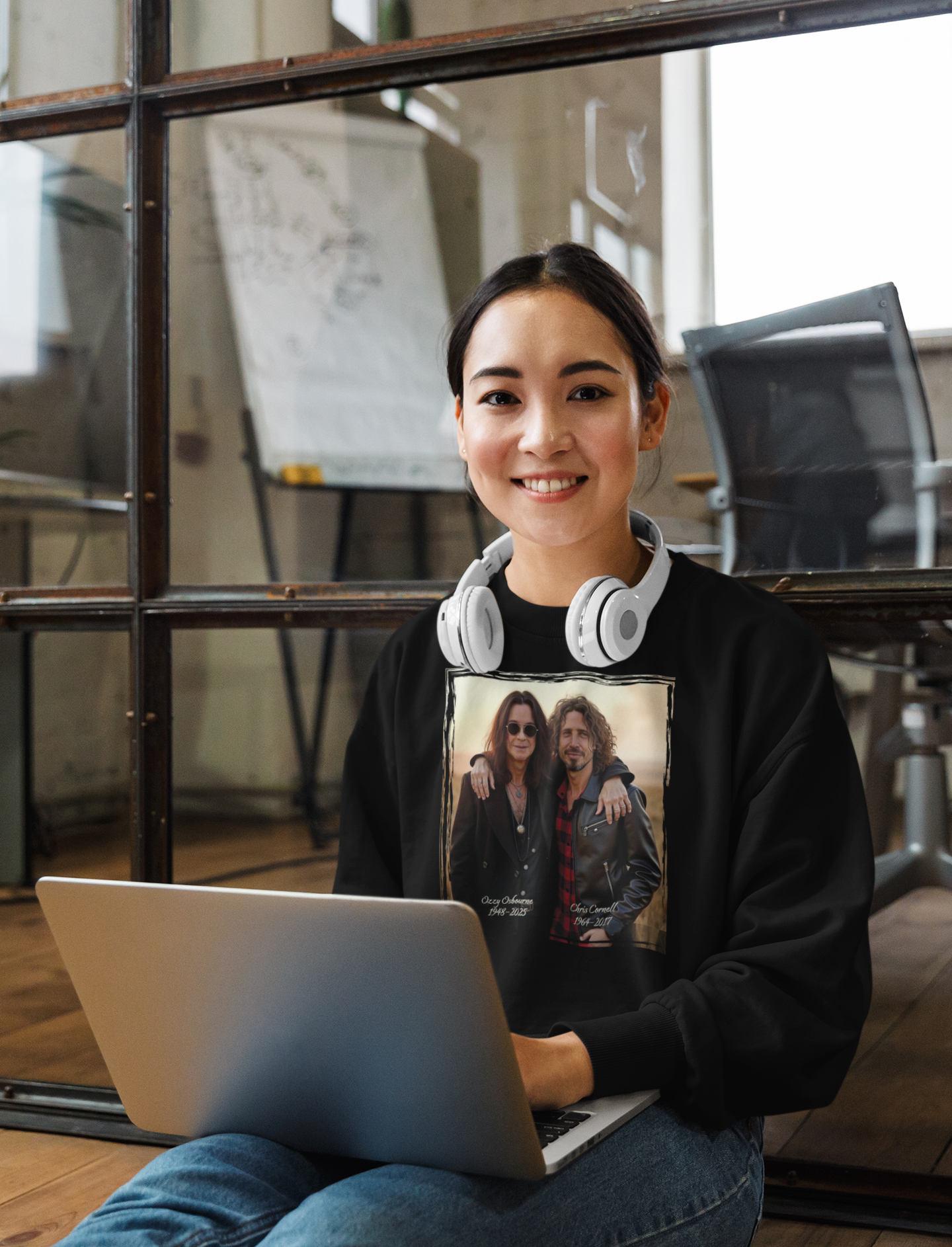 Person wearing a black sweatshirt with a graphic design of Ozzy Osborne and Chris Cornell sitting with a laptop in an office setting.