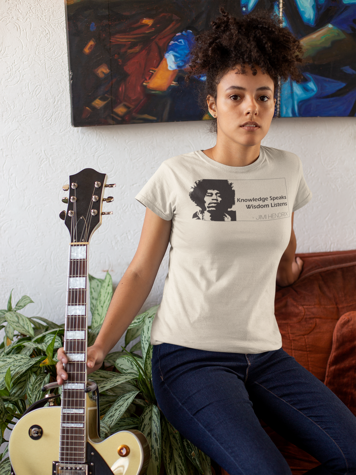 Person wearing a t-shirt with a graphic tee with the Jimi Hendrix quote Knowledge Speaks Wisdom Listens, holding an electric guitar in a casual setting.