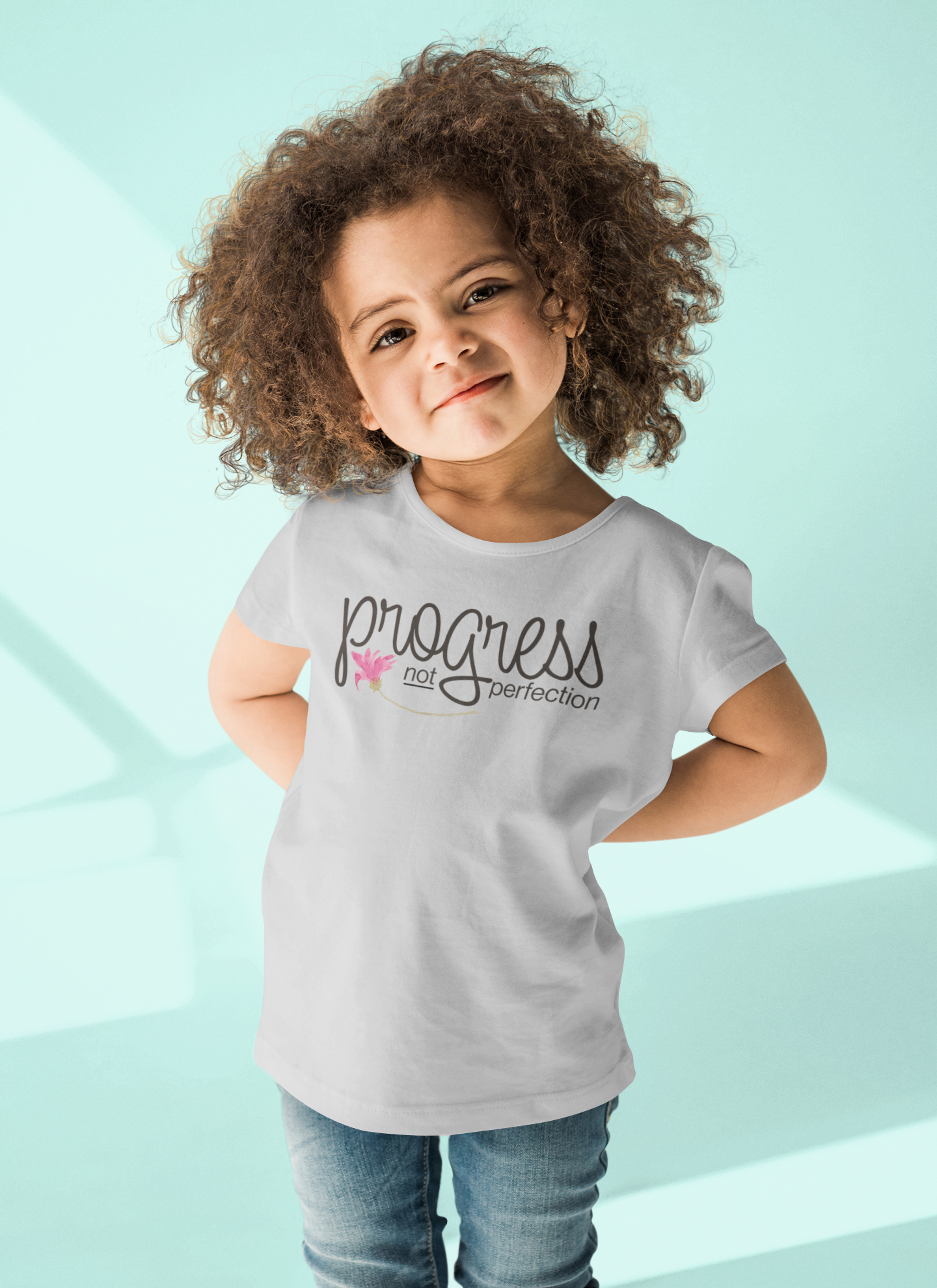 Child wearing a shirt with 'progress over perfection' text on a light blue background