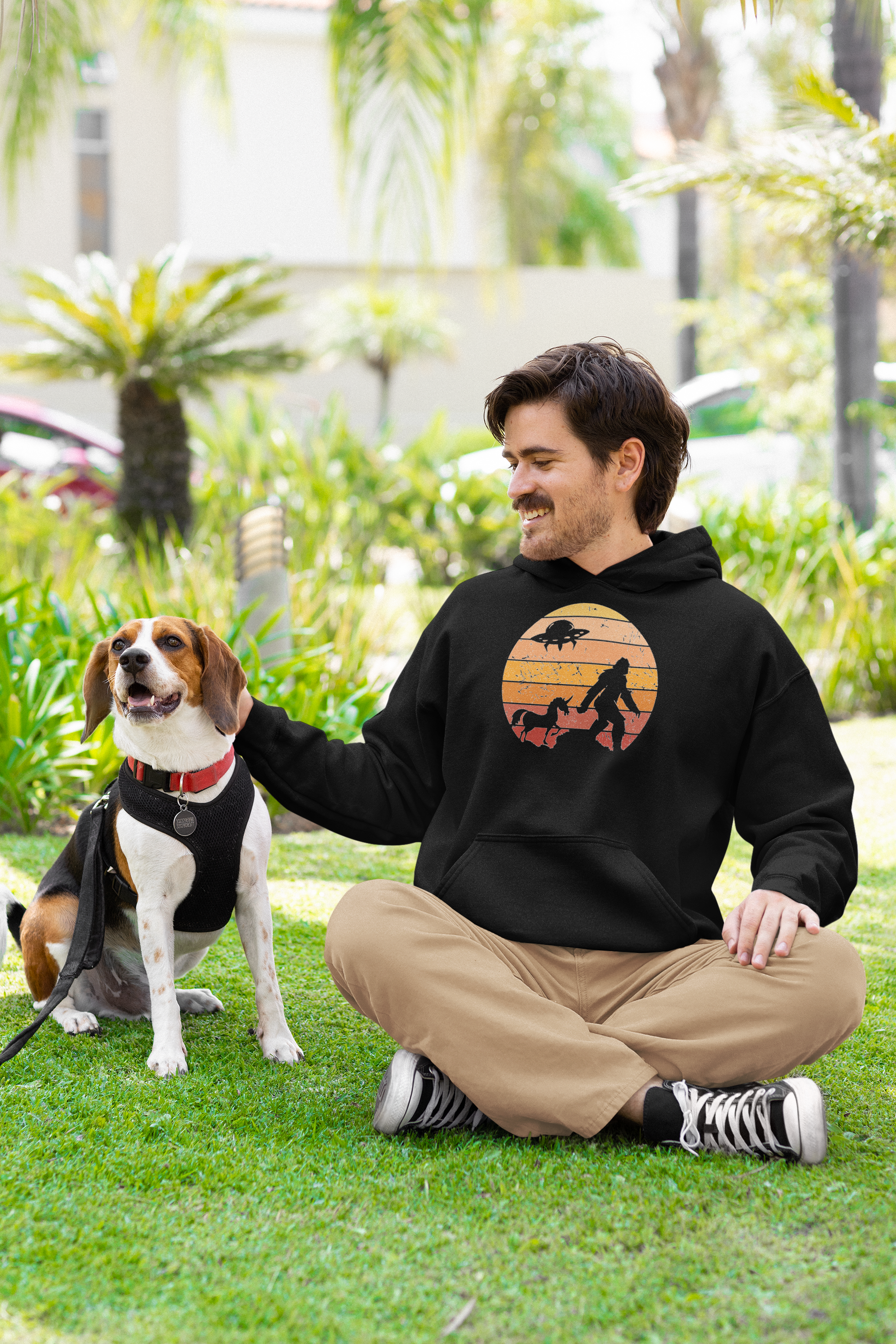 Man wearing a hoodie with Bigfoot, Unicorn and UFO against a sunset