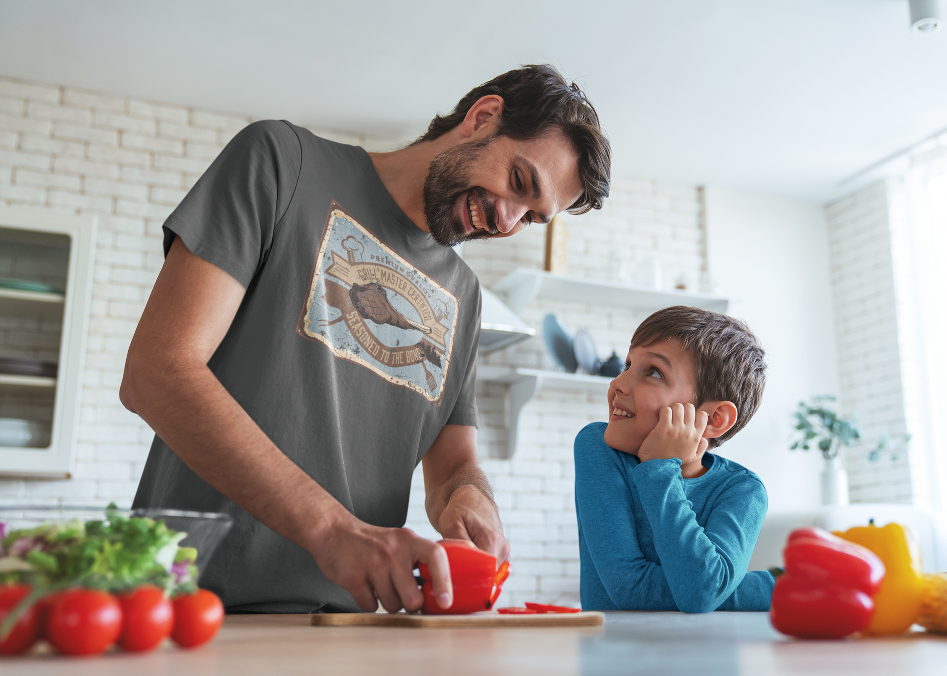 Man and child in a kitchen preparing food together. Man wearing a shirt that says Certified Grill Master. 