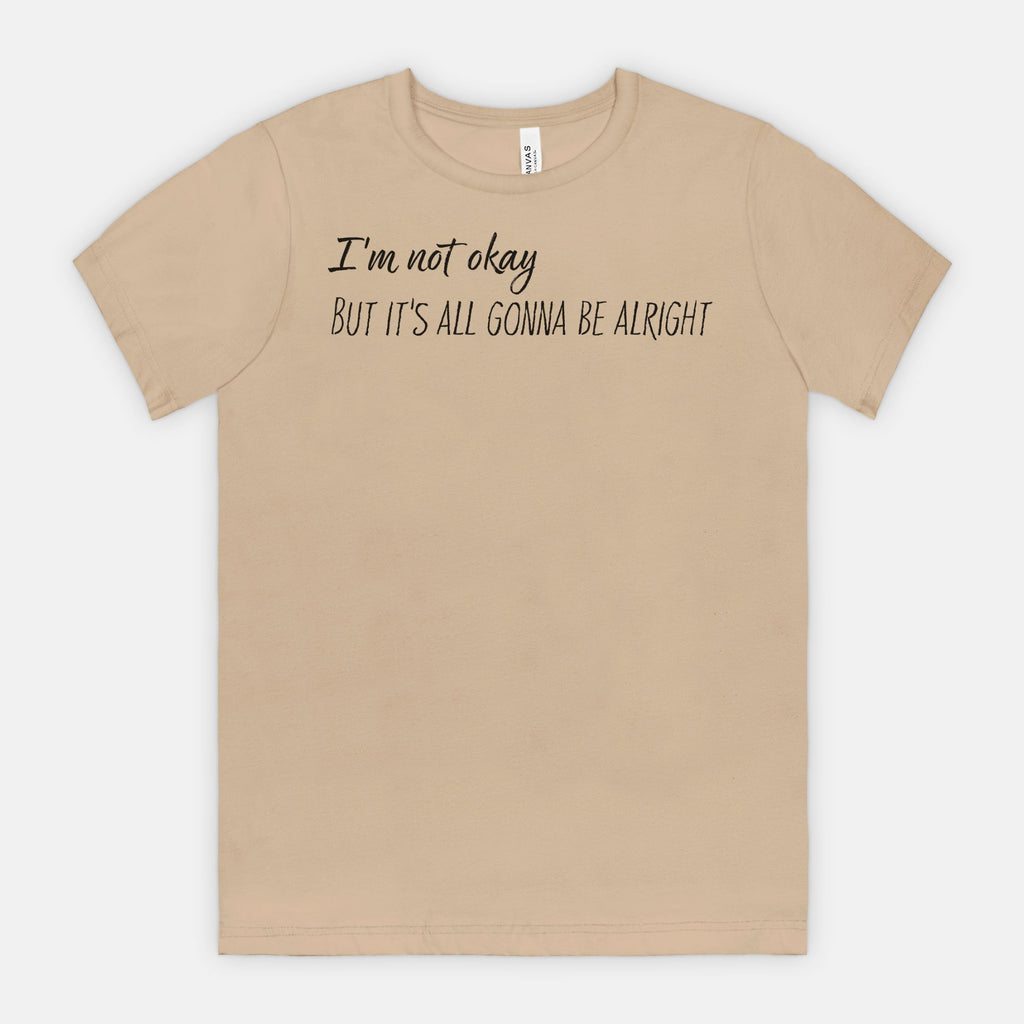Beige t-shirt with text 'I'm not okay, but it's all gonna be alright' on a white background
