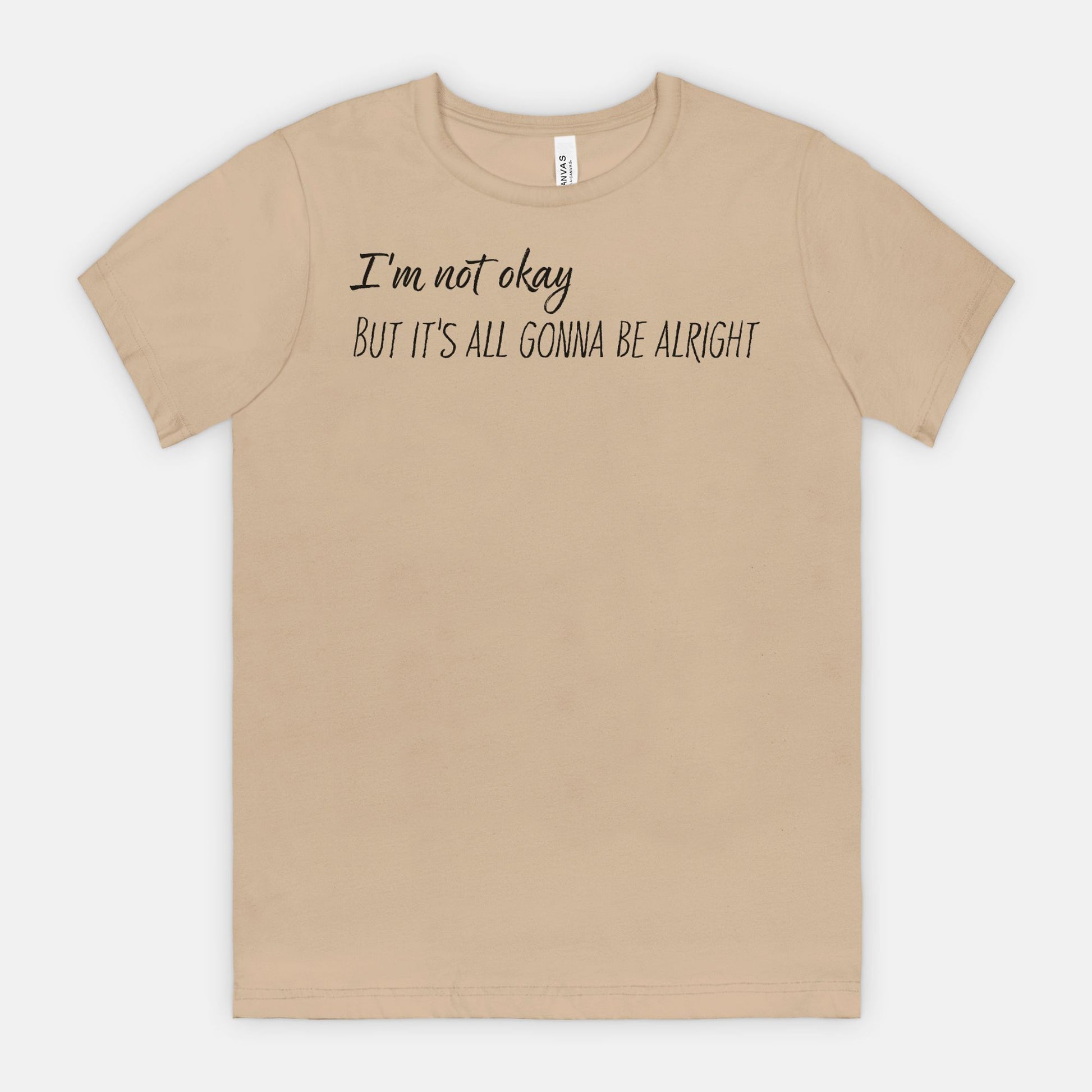 Beige t-shirt with text 'I'm not okay, but it's all gonna be alright' on a white background