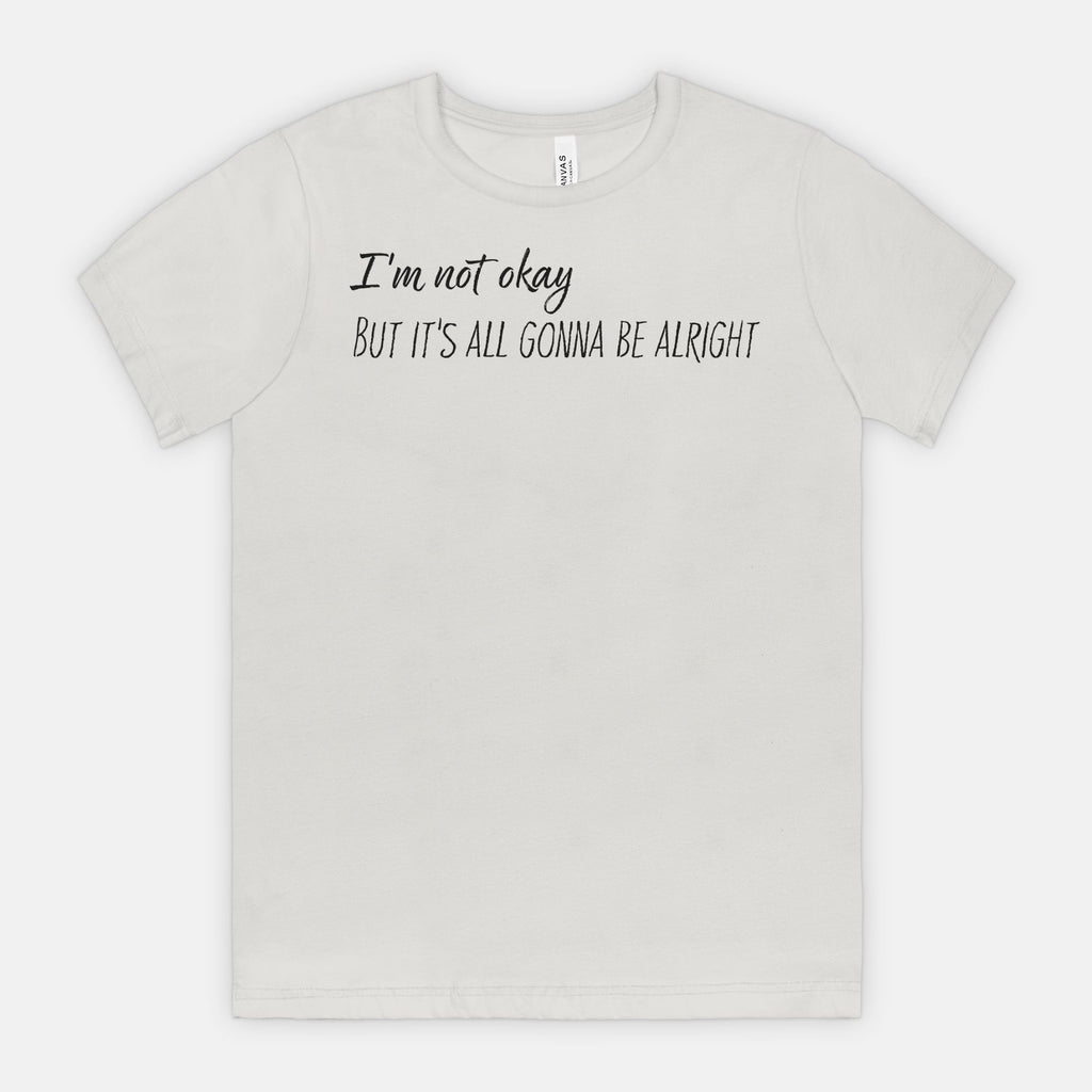 Silver t-shirt with text 'I'm not okay, but it's all gonna be alright' on a white background