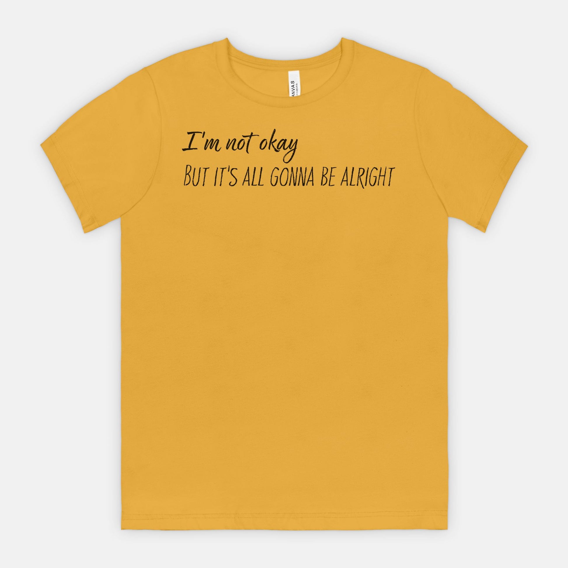 Mustard t-shirt with text 'I'm not okay, but it's all gonna be alright' on a white background