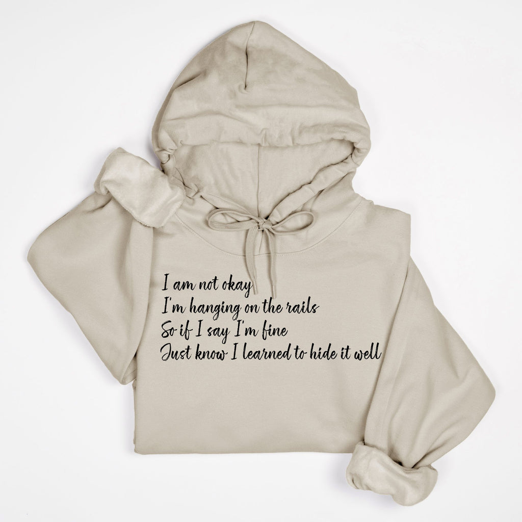 Beige hoodie with text "I am not okay hanging on the rails" on a white background