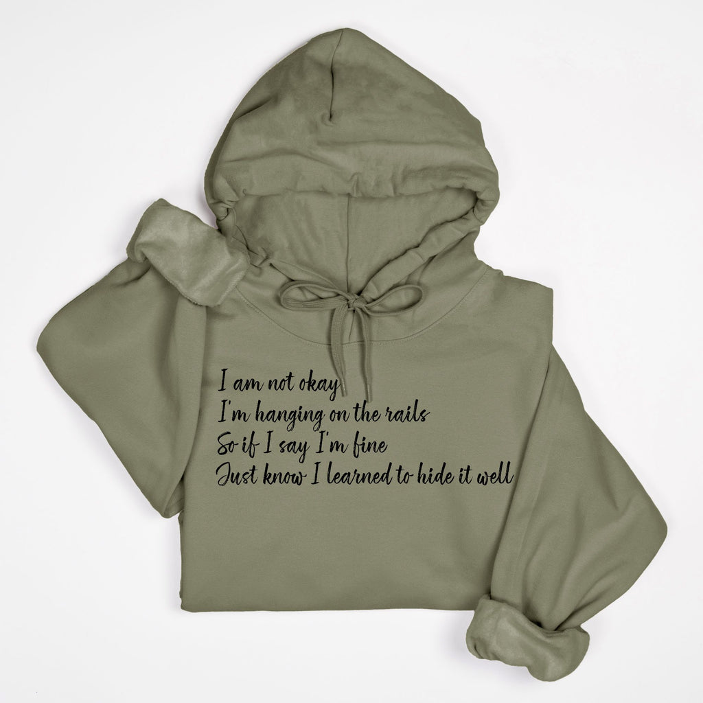 Sage green hoodie with text "I am not okay hanging on the rails"
on a white background