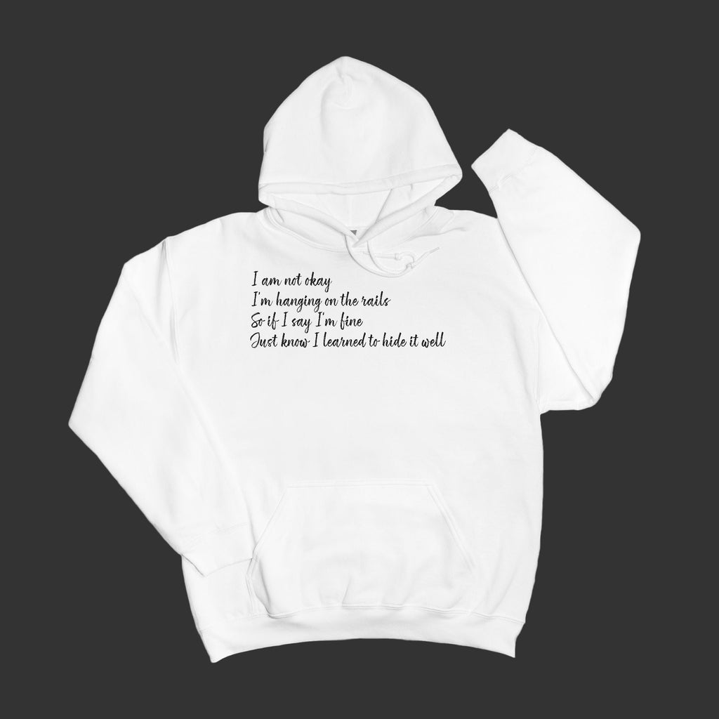 White hoodie with black text "I am not okay hanging on the rail" on a gray background