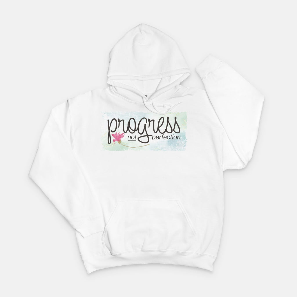 White hoodie with 'progress not perfection' text on a light gray background