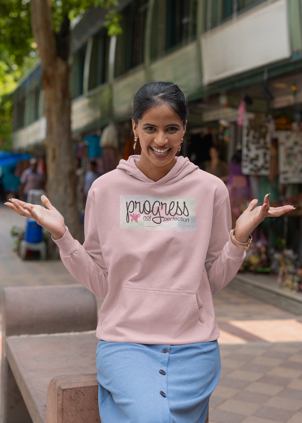 Woman wearing a pink hoodie with 'progress not perfection' text in an urban setting
