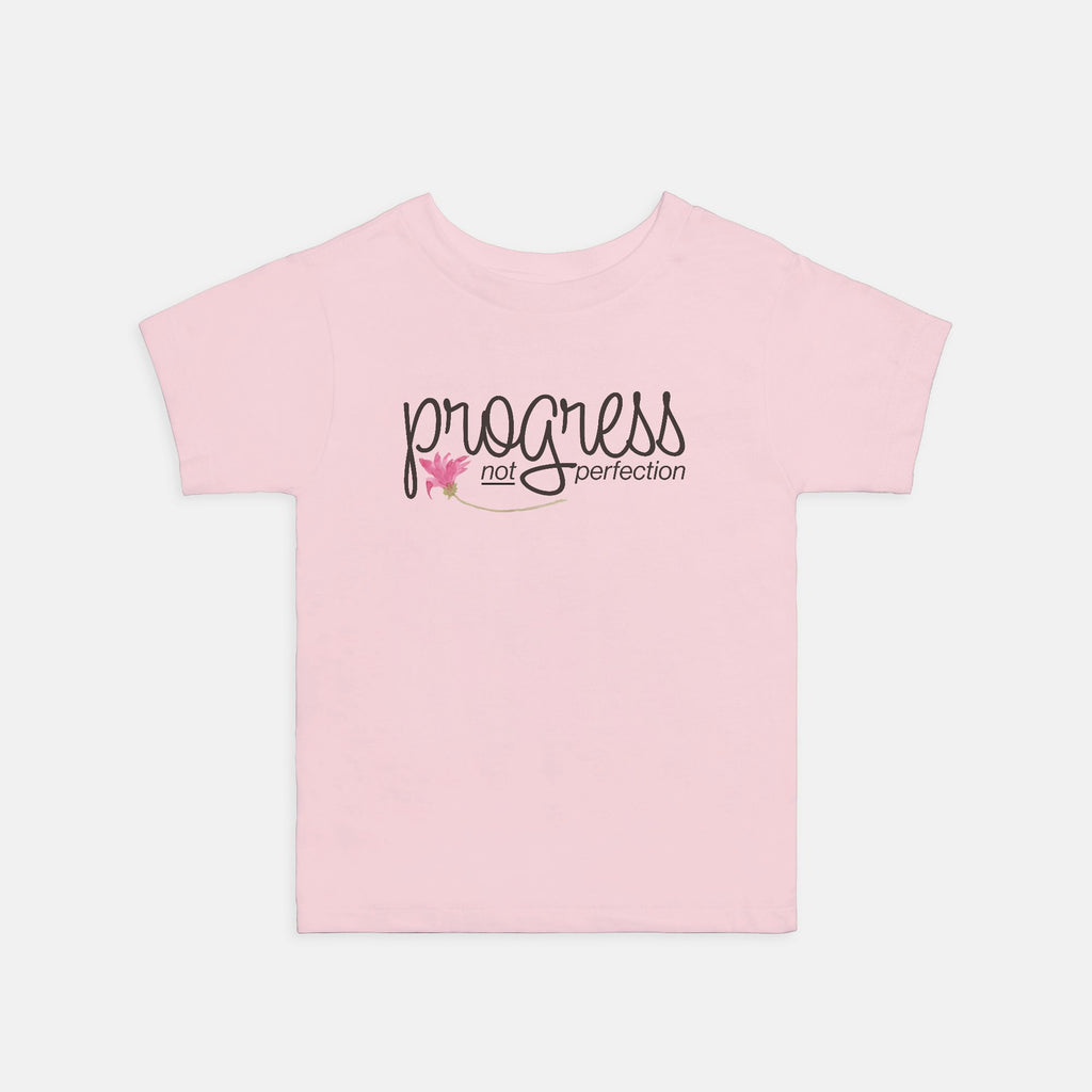 Pink t-shirt with 'progress not perfection' text on a light gray background