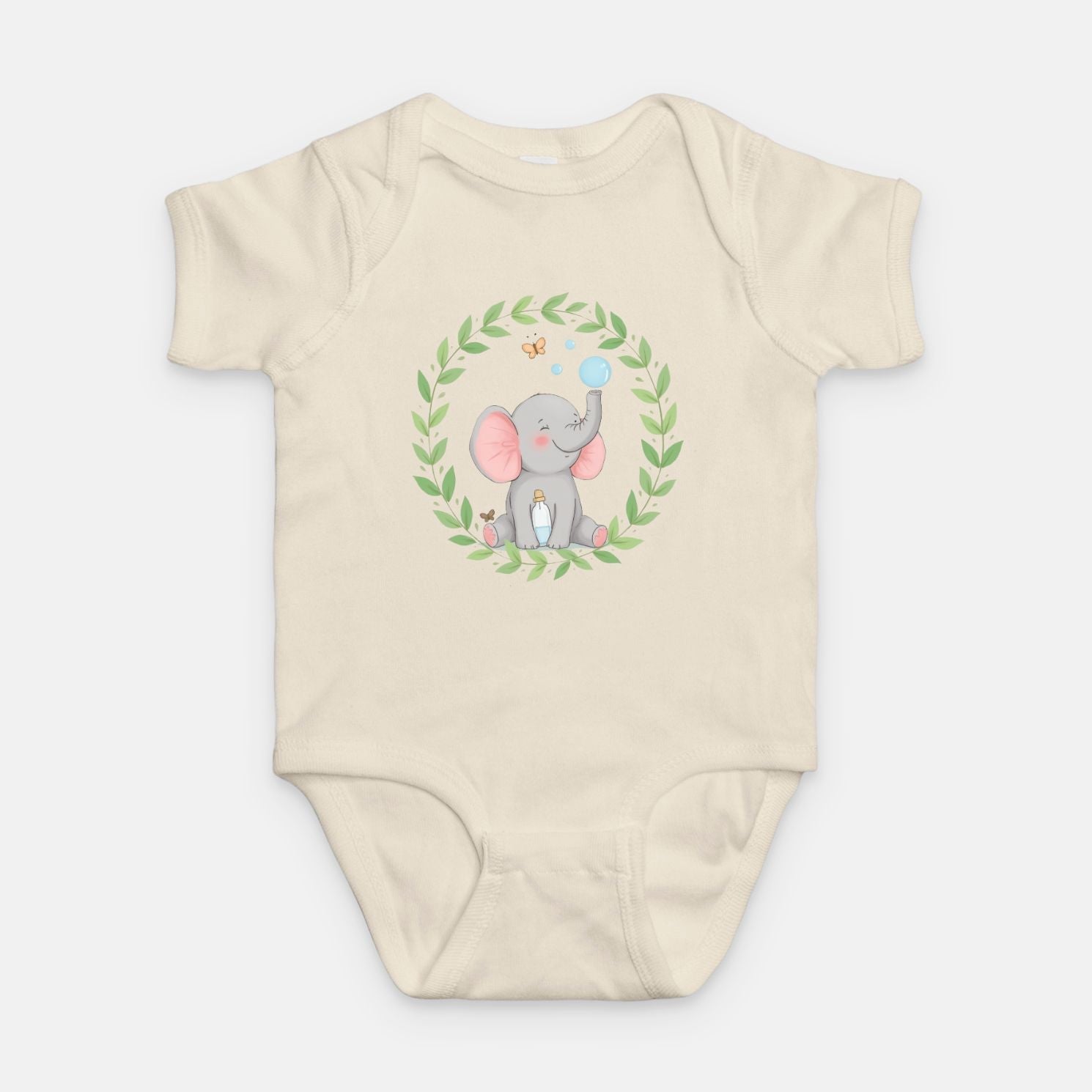 Little Chaos Crew elephant sitting with eyes closed, blowing bubbles beside a tipped bubble bottle inside green leafy wreath, minimalist baby cream onesie design.