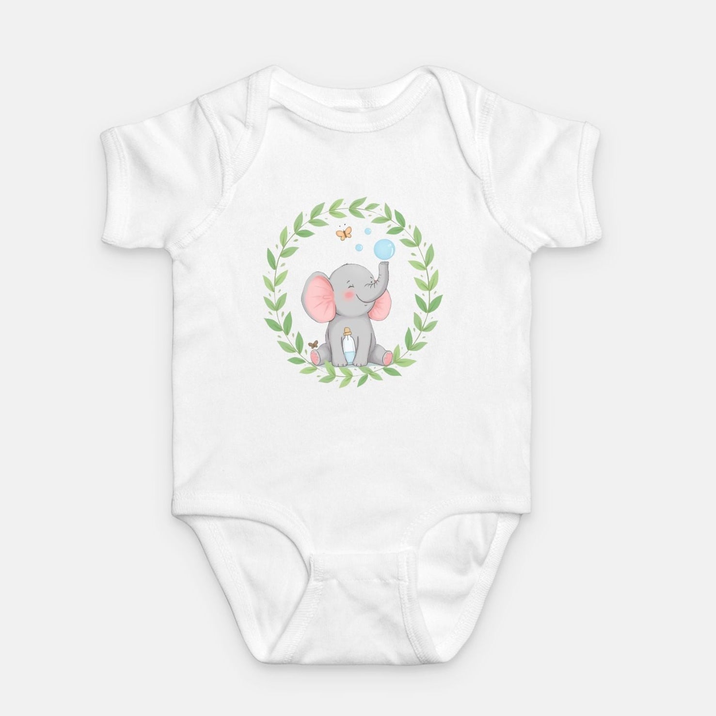 Little Chaos Crew elephant sitting with eyes closed, blowing bubbles beside a tipped bubble bottle inside green leafy wreath, minimalist baby white onesie design.
