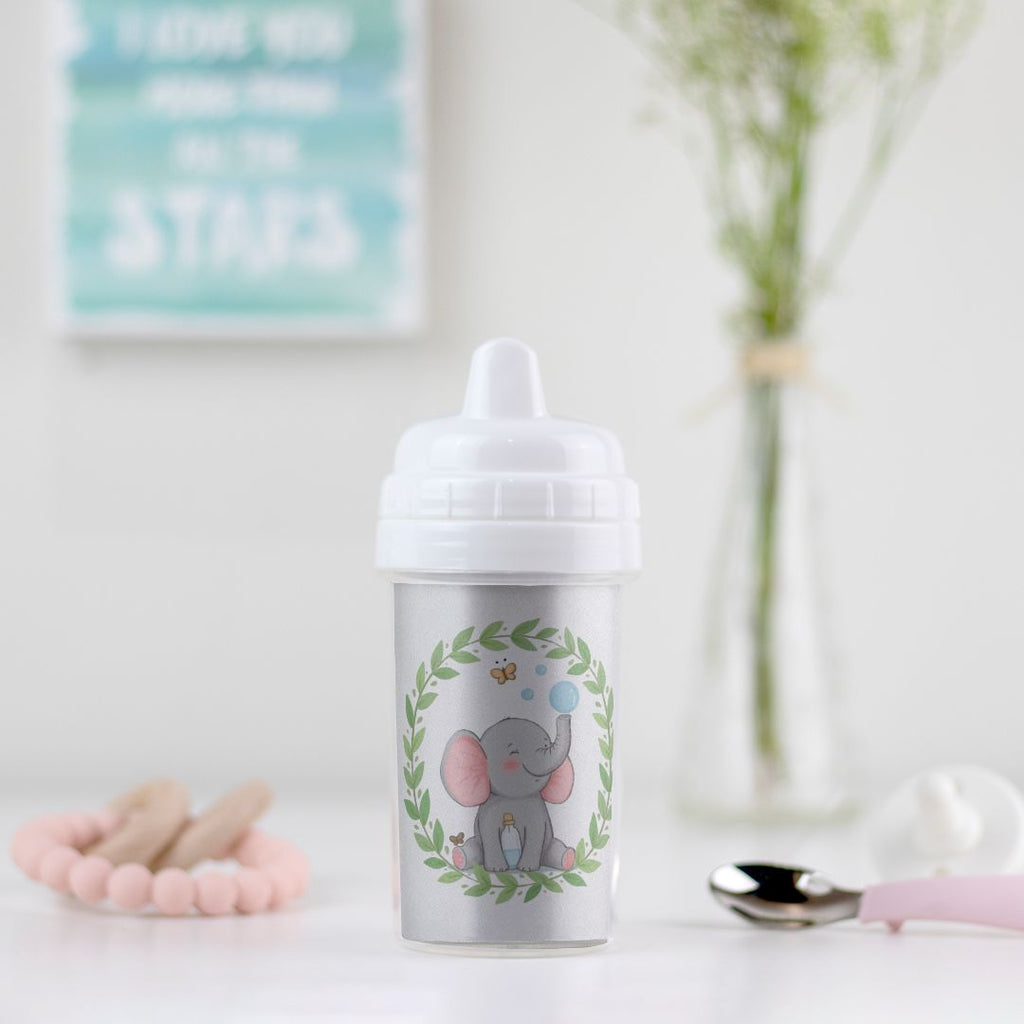 Little Chaos Crew elephant sitting with eyes closed, blowing bubbles beside a tipped bubble bottle inside a green leafy wreath on a toddler sippy cup.