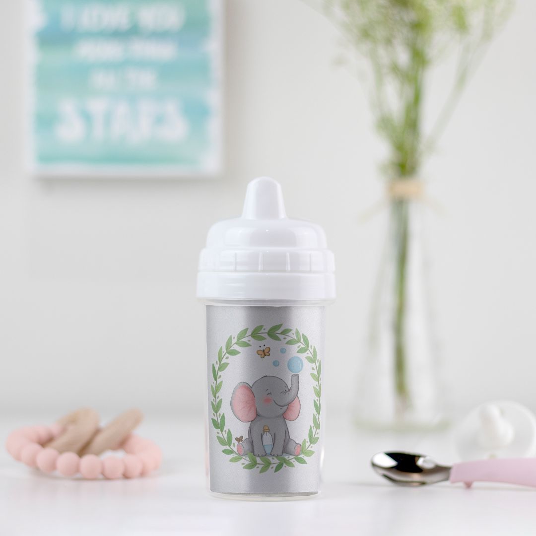 Little Chaos Crew elephant sitting with eyes closed, blowing bubbles beside a tipped bubble bottle inside a green leafy wreath on a toddler sippy cup.