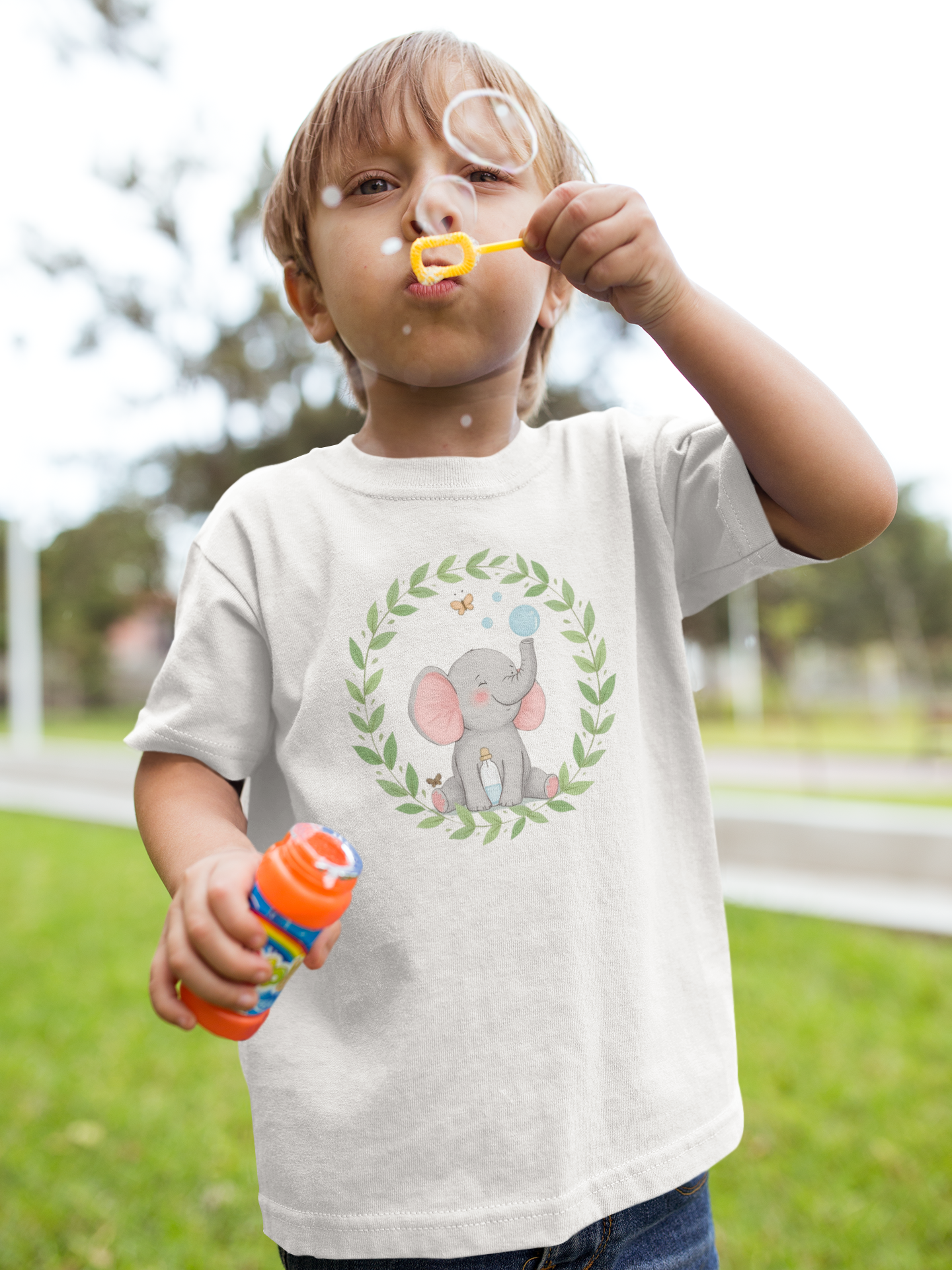 Little Chaos Crew elephant blowing bubbles beside a tipped-over bottle inside a green leafy wreath, minimalist toddler shirt design.