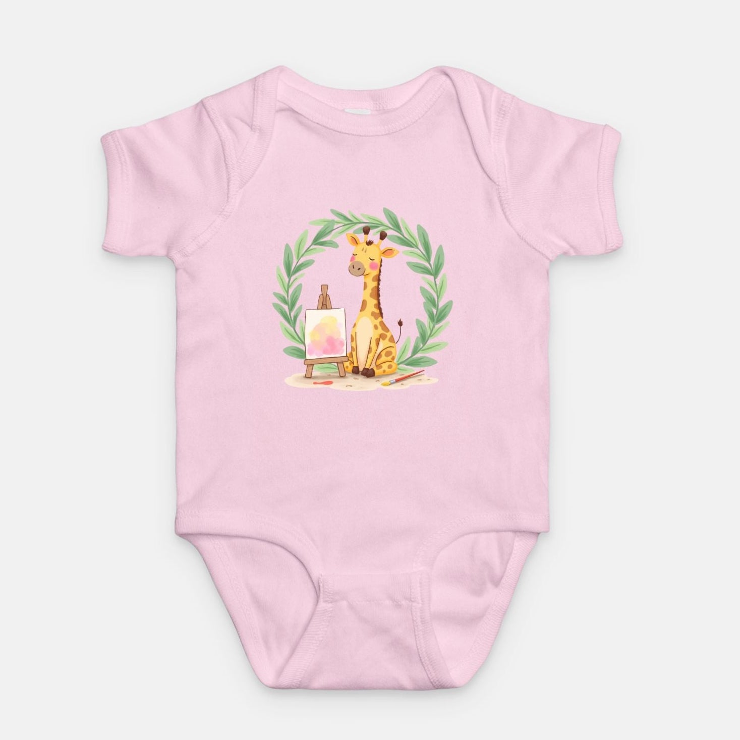 Little Chaos Crew giraffe sitting with eyes closed beside an easel and paintbrush inside green leafy wreath, minimalist baby pink onesie design.
