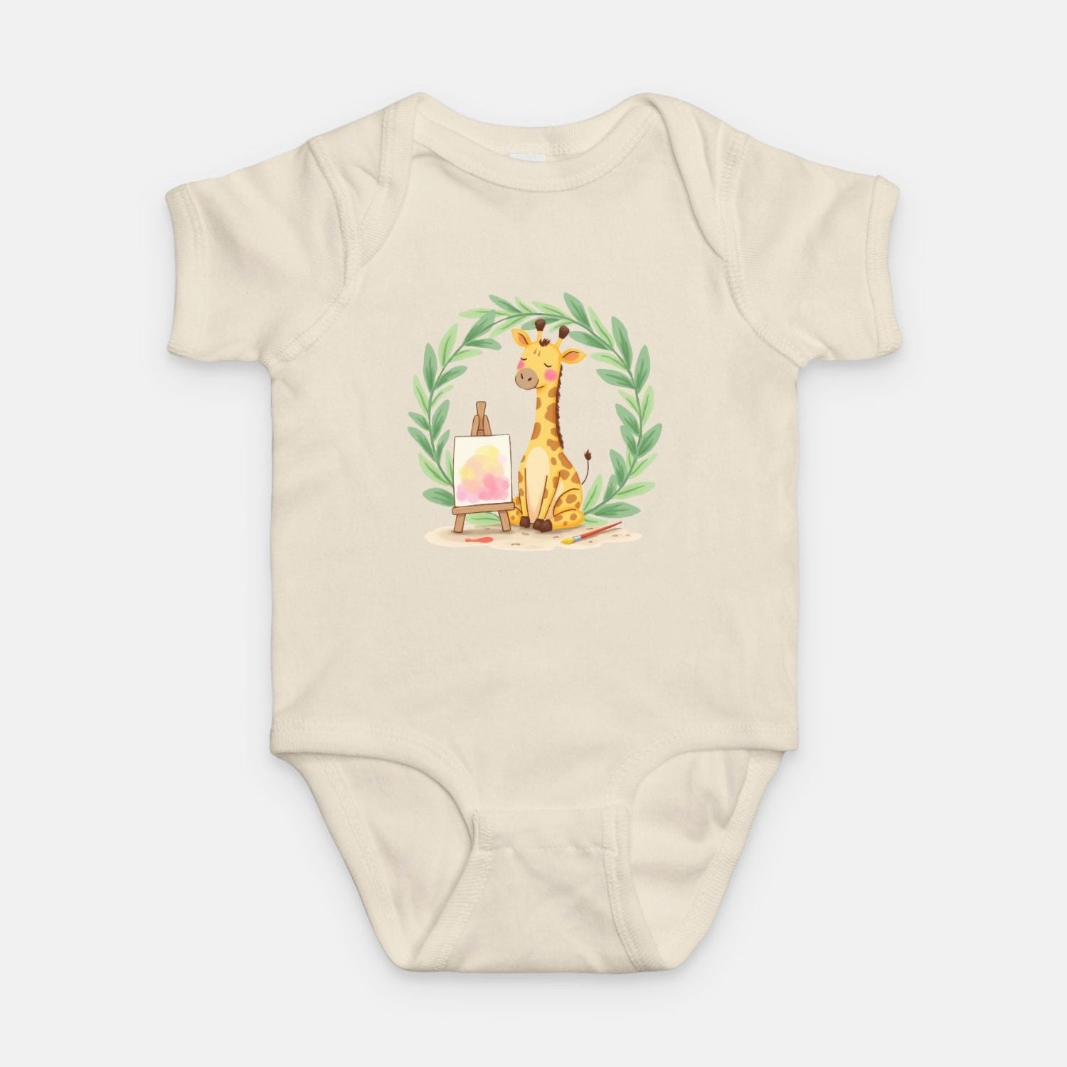 Little Chaos Crew giraffe sitting with eyes closed beside an easel and paintbrush inside green leafy wreath, minimalist baby cream onesie design.