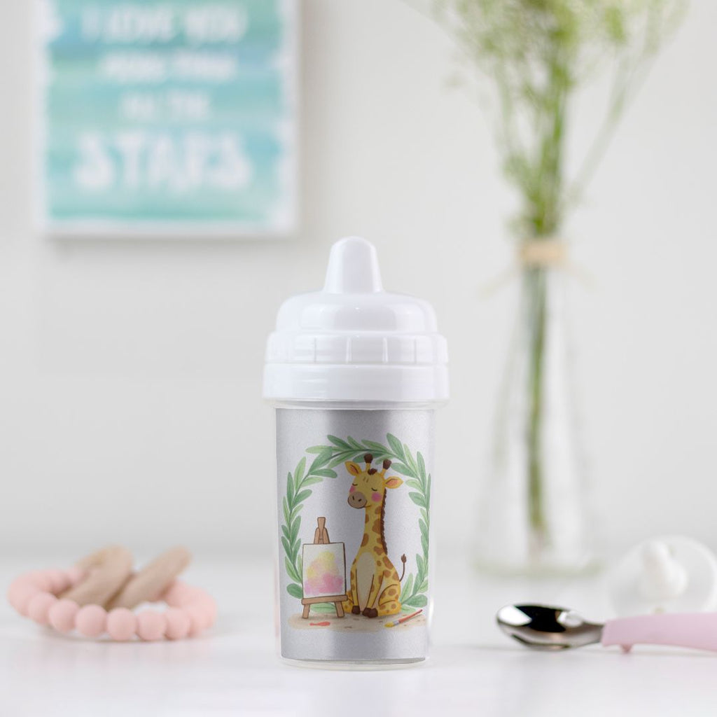 Little Chaos Crew giraffe sitting with eyes closed beside an easel and paintbrush inside a green leafy wreath on a toddler sippy cup.